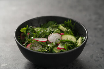 Summer fresh salad with radish, cucumber and herbs in black bowl