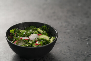 Summer fresh salad with radish, cucumber and herbs in black bowl