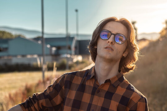 Joven con gafas mirando a camara al atardeccer. Joven con camisa de ecuadros. Chico veraneando.