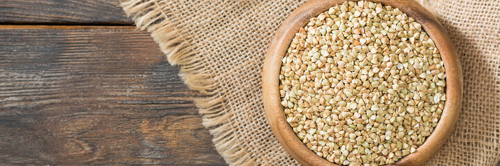 Green buckwheat in a wooden bowl on a brown wooden table. Superfood in a bowl. Green buckwheat close-up. The view from the top. Banner with space for text