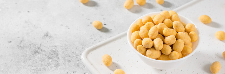 Fried peanuts in cheese sauce in a white bowl on a light gray table. Banner with space for text