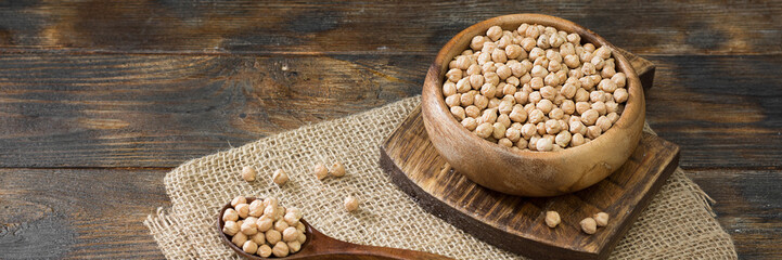 Chickpeas in a wooden bowl on the brown kitchen table. Raw chickpeas close-up. Banner with space for text