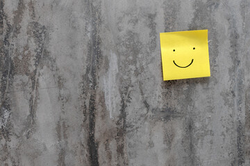 Yellow sticker note paper with drawn smiley on cement background. Sticky note.