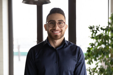 Close up headshot portrait of smiling young Arabic businessman in glasses pose at workplace,...