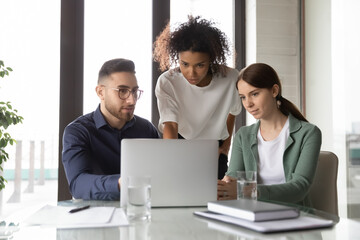 Concentrated multiracial businesspeople gather in boardroom look at computer screen brainstorm over...