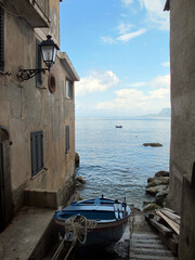 Fototapeta na wymiar A picturesque view of a narrow street resting in the sea, with houses partly in the water, a boat moored against the wall of the house with windows, shutters, a beautiful lantern against the blue sky 