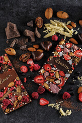 Fototapeta na wymiar black and milk chocolate with handmade freeze dried berries and nuts, natural on a dark background, top view