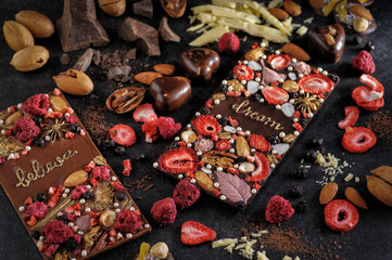 Obraz na płótnie Canvas black and milk chocolate with handmade freeze dried berries and nuts, natural on a dark background, top view