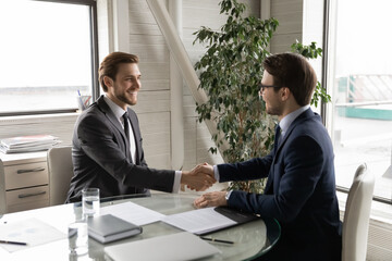 Happy excited Caucasian young businessmen handshake get acquainted greeting at office meeting, smiling male boss shake hand congratulate colleague employee with promotion, employment concept