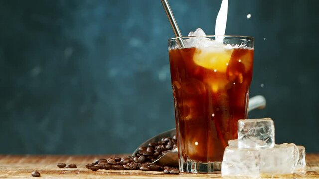 Slow motion pouring cold brew iced coffee into a glass over ice cubes
