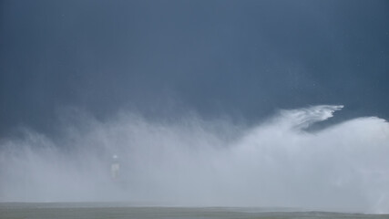 Naklejka na ściany i meble Massive waves crash over harbour wall onto lighthouse during huge storm on English coastline in Newhaven, amazing images showing power of the ocean