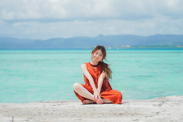 沖縄の青い海とオレンジのワンピースを着た女性