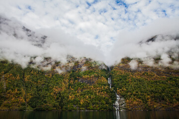 Low clouds over a waterfall in Geiranger fjord  in Norway