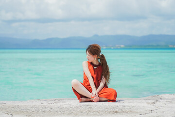 Fototapeta na wymiar 沖縄の青い海とオレンジのワンピースを着た女性