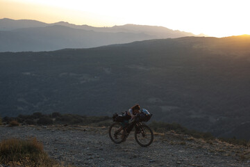 A bikepacker pushes her bike uphill at dusk. 