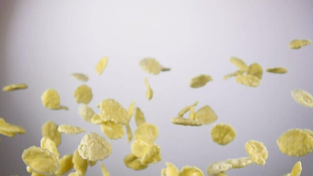 Cereal corn flakes are bouncing up on the white background in the slow motion