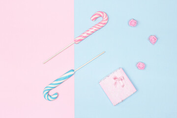Two candy canes with gift box on pastel blue and pink background. Top view, flat lay. Congratulation feminine minimal concept