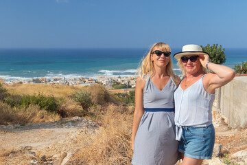 Smiling daughter and mother stand behind their backs panorama of the city beach and the sea.