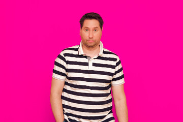 Irritated man 35 40s in striped t-shirt standing look isolated over magenta background