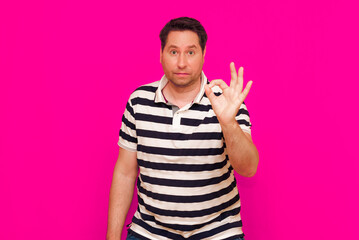 Fototapeta premium Brunette young man in striped t-shirt showing ok sign isolated over magenta background
