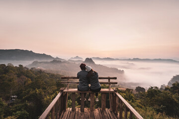 Young couple traveler looking at sea of mist and sunset over the mountain at Mae Hong Son, Thailand