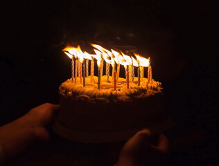 Anniversary cake with burning candles on dark background