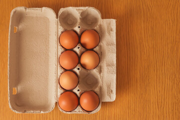 A cardboard box from the store with brown chicken eggs stands on a wooden table. The view from the top.