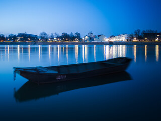 Fototapeta na wymiar Blue hour on Sava river, promenade in Slavonski Brod and blurred boat in front.