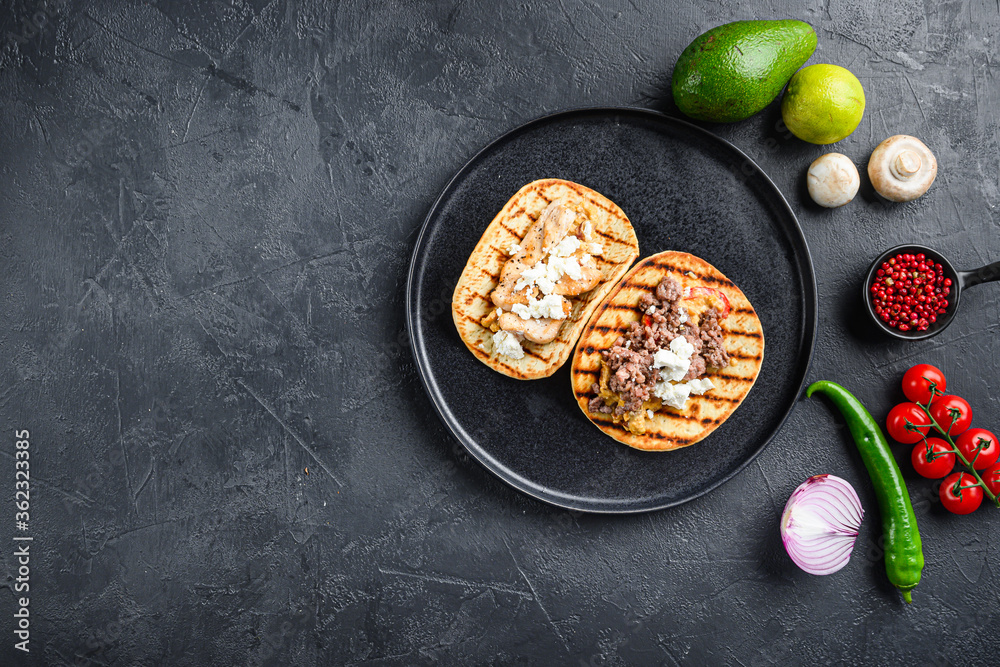 Wall mural Mexican tacos with vegetables and beeaf and chicken meat on black round plate over textured black background, top view with space for text. - Wall murals