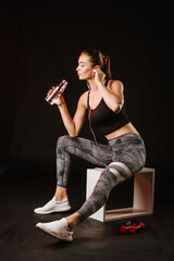 Slim sporty woman relax after training with bottle of water on black background