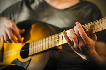 Fototapeta na wymiar A man in a gray t-shirt plays a tune on a decrepit old acoustic guitar, illuminated by the light.