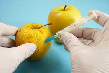 apple in genetic engineering laboratory with syringe and test tubes on blue background, gmo food...