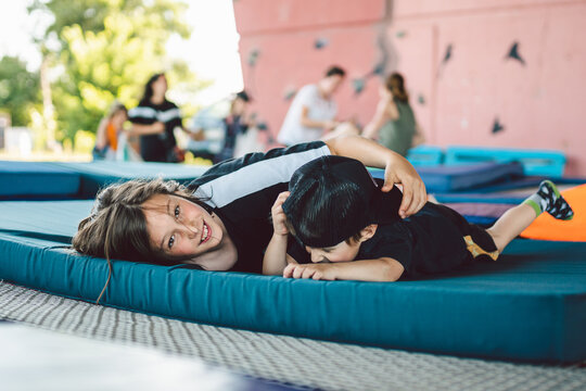 Happy children playing lying on trampoline. Brothers are having fun lying on a sports mat on a trampoline in the gym outside. Boys indulge, laugh and hug each other after training