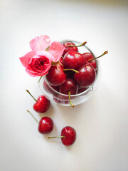 In a glass glass a ripe cherry with a rose flower isolated on a white background