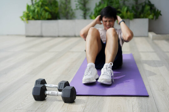 close up dumbbell with young man in sit-up pattern on the floor to workout alone in the morning at home's rooftop  for quarantine lifestyle and healthy concept	