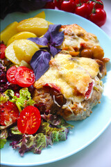 On a plate a dish of meat with slices of potatoes and cherry tomatoes