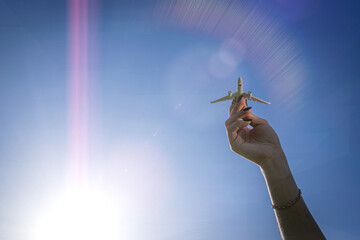 Air plane wings in sun light sky. White airplane toy in girl hand fly on bright sunlight background. Aircraft flight travel concept.
