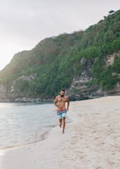 a man with a beard and naked torso runs along the beach barefoot