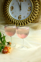 Two glasses of a pink cocktail or champagne drink, a golden watch (five minutes to twelve), a rose....