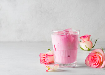 Ice rose latte in glass with pink flowers and petal on white or grey background - obrazy, fototapety, plakaty
