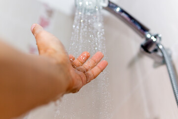 hands check the temperature of the shower water. a man's hand under a stream of water selective...