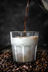 Pouring coffee into a glass of milk with coffee beans background