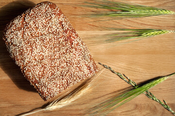 Composition rye bread in form of  brick with sesame topping and spike of wheat on brown wooden...
