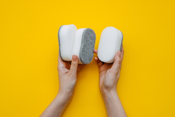 Fototapeta na wymiar Human hands holding minimalist white dish sponges on bright yellow background. Concept of cleaning.