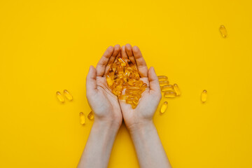 Human hands holding a bunch of fish oil capsules on bright yellow background.