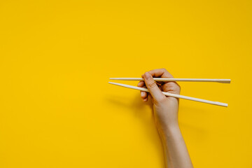 Human hand using chopsticks, on clean yellow background. Learning how to use chopsticks.