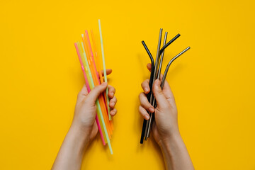 Human hands holding metallic and plastic straws on clean yellow background. Concept of zero plastic...