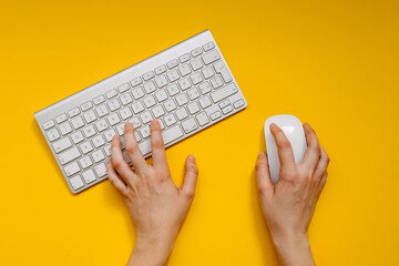 Hands typing on a wireless keyboard and holding a wireless mouse on clean yellow background.