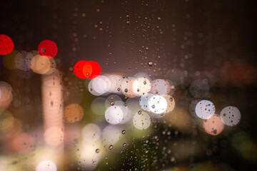 Raindrops on the window glass at night against the background of bokeh from the lights and Windows of the houses opposite