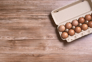 Raw chicken eggs in cardboard box on brown wooden background with copy space. Top view.
